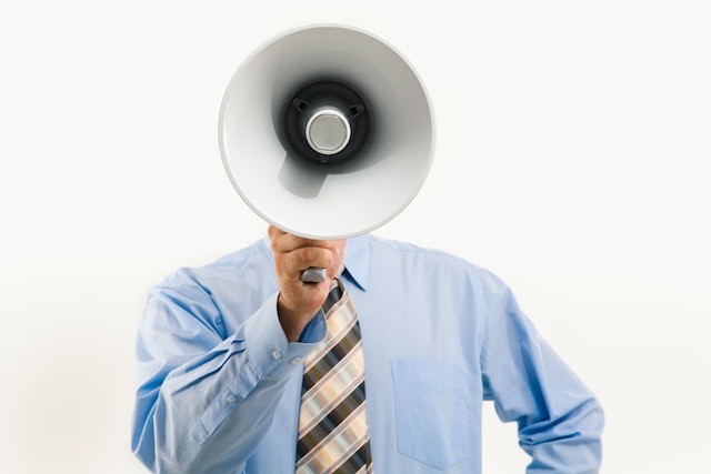 person wearing a blue shirt and tie holding a megaphone in front of their face